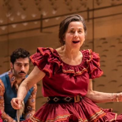 Liza Sadovy as Aunt Eller dancing in a red rufflled dress, which is swaying with the movement.